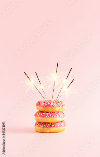 Doughnut cake with sparklers on a pink nbackground. Minimal composition. Party creative idea. photo