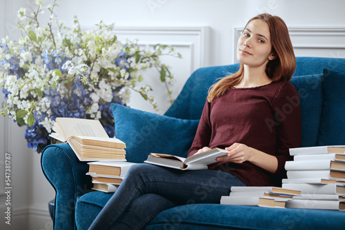 Young pretty woman is sitting on a sofa among a stack of books.