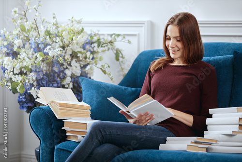 Obraz na płótnie Young female book lover is sitting on a sofa among a stack of books. w salonie