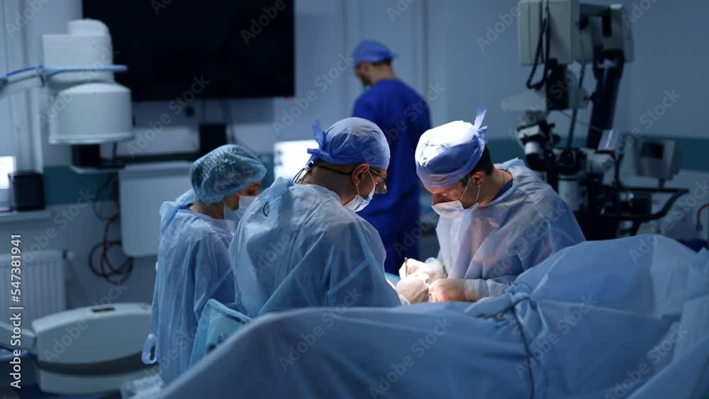Experienced team of neurosurgeons working in the surgery room. Doctors sit near the patient performing operation. Experienced team of neurosurgeons working in the surgery room. Doctors sit near the patient performing operation.