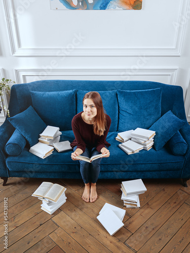 Obraz na płótnie Young surprised woman among stacks of books on a sofa in the living room. w salonie
