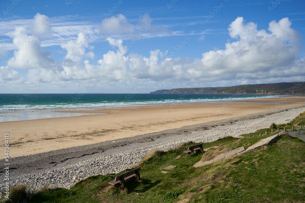 Landscape in the Normandy. Blue sea with waves in front of stony sand beach. Hills under blue cloudy sky. Nobody. France, Normandy, Manche, Vauville. Landscape in the Normandy. Blue sea with waves in front of stony sand beach. Hills under blue cloudy sky. Nobody. France, Normandy, Manche, Vauville.