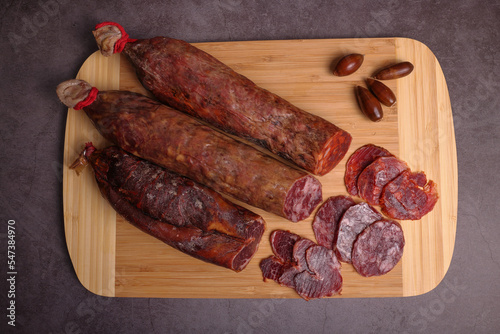 Iberico sausage, Iberico chorizo and Iberico loin on cutting board and dark gray table, garnished with acorns