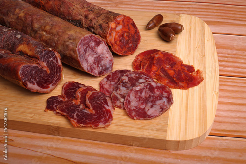 Iberian sausage, Iberian chorizo and Iberian loin on cutting board and wooden table, garnished with acorns photo