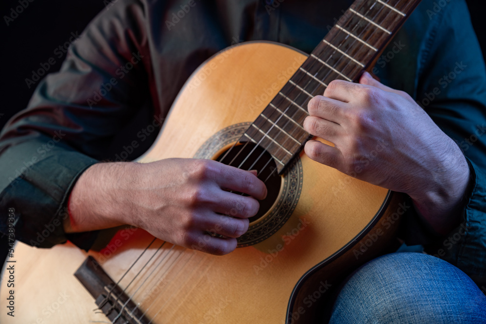 Fototapeta premium The guy in the dark shirt is plucking the strings of a six-string guitar