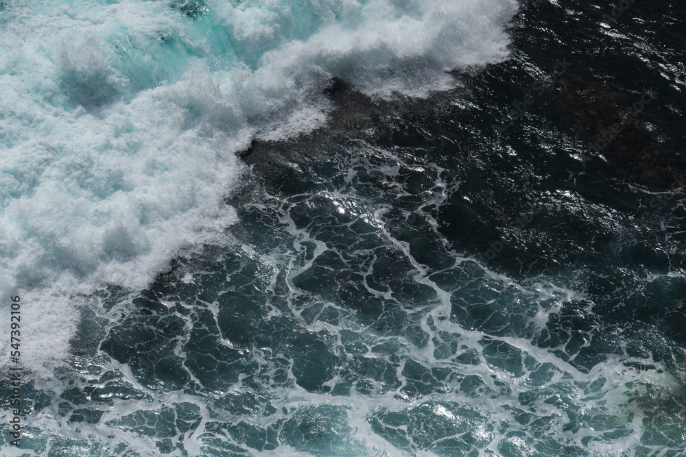 The waves of the ocean water meet with underwater pointed rocks