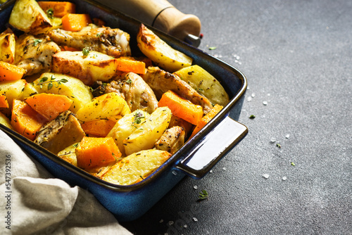 Chicken meat with pumpkin and potato at dark background. One pot baked dish.