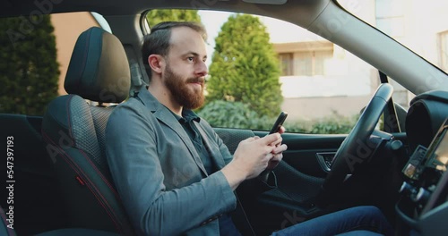 Serious business man working with cellphone in modern car. Focused male professional chatting using phone at car. Man writing message on mobile phone in business car.