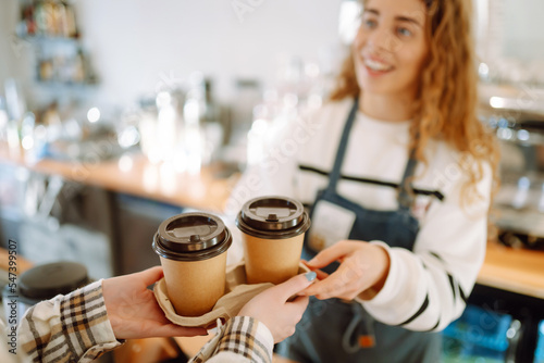 Smiling barista- girl giving take away coffee cups to a customers. 