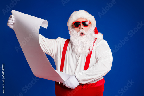 Portrait of his he attractive amazed fat white-haired Santa holding in hands reading wish present gift list pout lips order isolated bright vivid shine vibrant red burgundy maroon color background photo