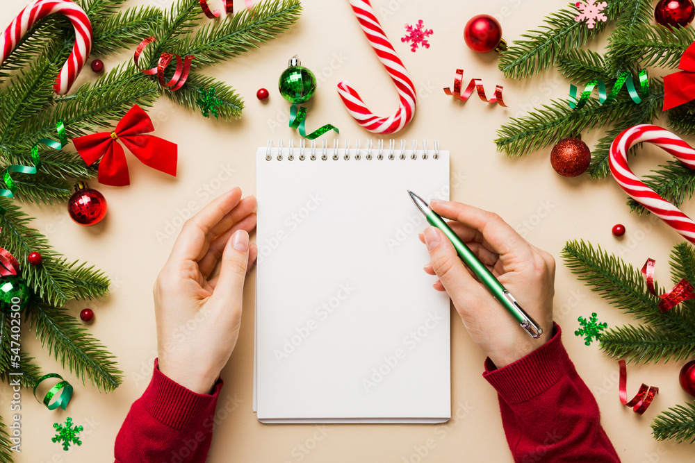 Woman writing Christmas to do list on notebook on colored ...