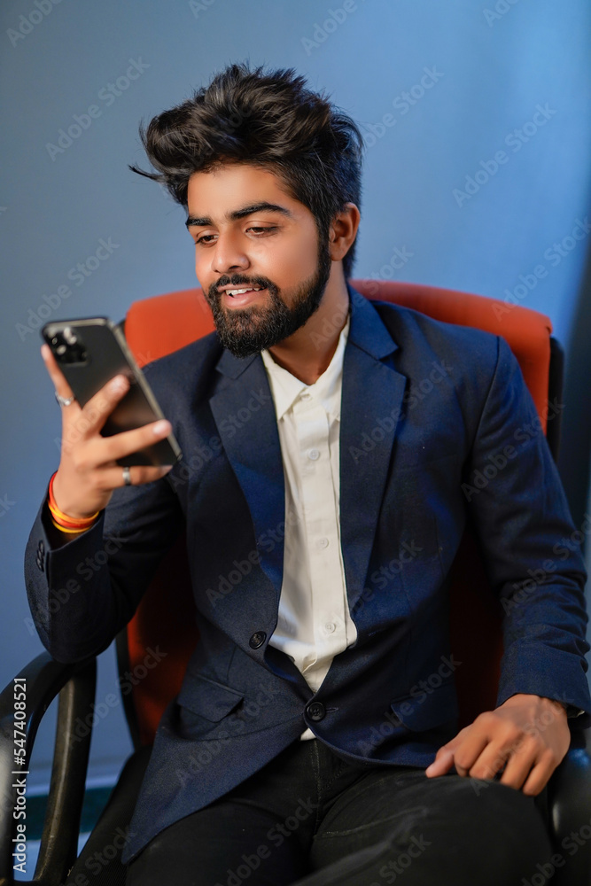 Naklejka premium Businessman sitting on chair isolated. Handsome young indian businessman using mobile phone, confident smile looks. half shot.