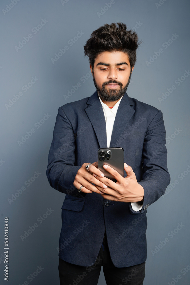 Portrait of a handsome happy young businessman wearing suit standing isolated over gray background, using mobile phone, video call concept Portrait of a handsome happy young businessman wearing suit standing isolated over gray background, using mobile phone, video call concept
