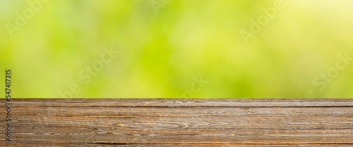 Background with blurred green leaves and empty wooden planks in the foreground.