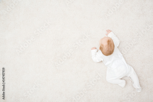 Papier peint Baby in white bodysuit crawling on knee and arms on light beige home carpet background