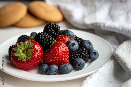 Closeup of a Composition with berries on a white plate and sweet cookies in the background