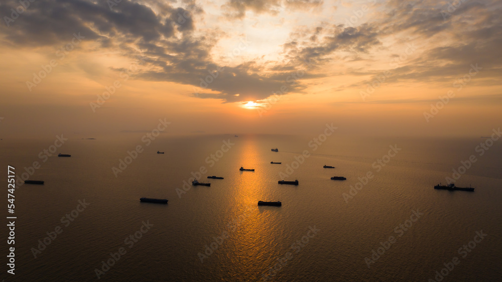 Silhouette group of Container ship floating in middle sea and over the sunset background at evening, photograph from drone point of view,