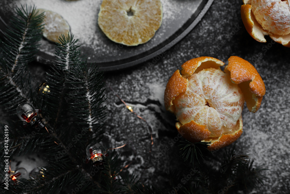 sweet orange juicy tangerines in a peeled peel lie on a black background and a black kitchen tray next to a spruce Christmas branch and sprinkled with white powder.for cards, banners, flyers, invitati sweet orange juicy tangerines in a peeled peel lie on a black background and a black kitchen tray next to a spruce Christmas branch and sprinkled with white powder.for cards, banners, flyers, invitati
