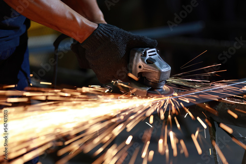 Senior cutting, grinding and polishing metal part with sparks indoor workshop, close-up.