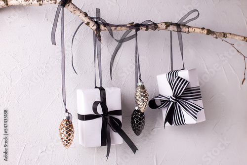 Wrapped black and white boxes with presents and decorative cones hanging on a branch against textured background. Scandinavian style. Place for text.