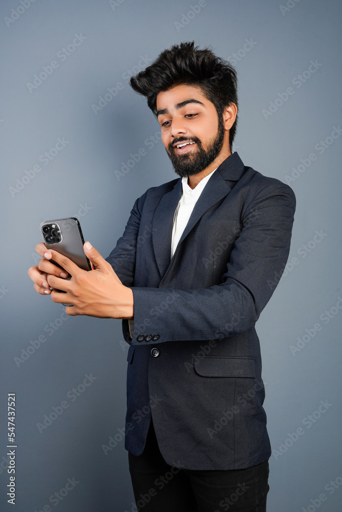 Portrait of a handsome happy young businessman wearing suit standing isolated over gray background, using mobile phone, video call concept Portrait of a handsome happy young businessman wearing suit standing isolated over gray background, using mobile phone, video call concept