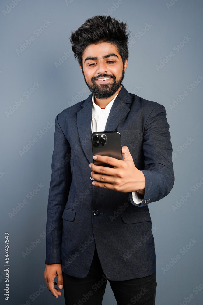 Portrait of a handsome happy young businessman wearing suit standing isolated over gray background, using mobile phone, video call concept Portrait of a handsome happy young businessman wearing suit standing isolated over gray background, using mobile phone, video call concept