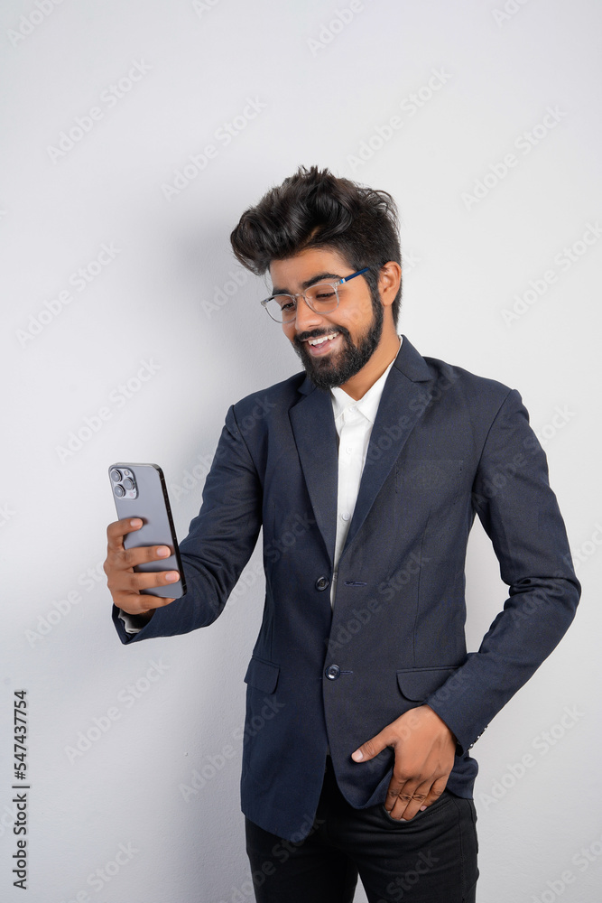 Portrait of a handsome happy young businessman wearing suit standing isolated over gray background, using mobile phone, video call concept Portrait of a handsome happy young businessman wearing suit standing isolated over gray background, using mobile phone, video call concept