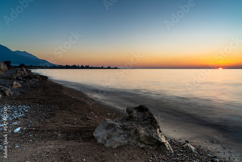 peaceful sunset over the ocean with silhouette of mountains and pebble beach iwth rock boulders in the foreground