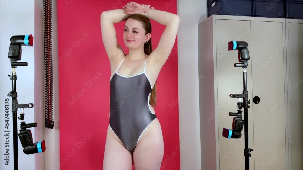 Beautiful sporty girl in white metallic one piece swimsuit at photo shoot in studio in time lapse