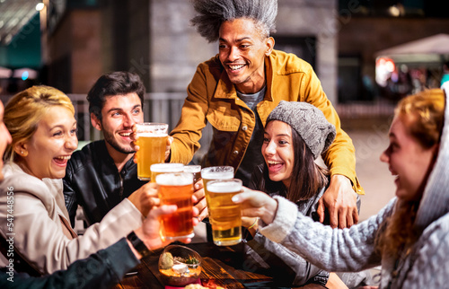 Happy friends drinking beer at brewery bar garden out door - Multiracial life style concept with genuine people enjoying time together eating at restaurant patio - Vivid filter with focus on mid guy