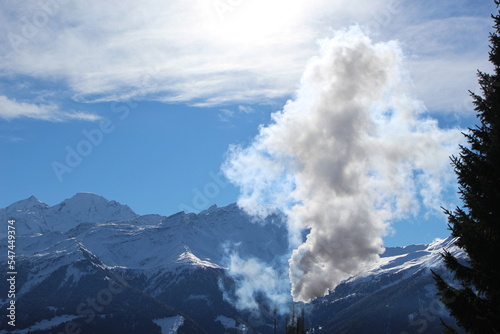 Steam coming from a smokestack seen in a mountain landscape. Snow covered mountains