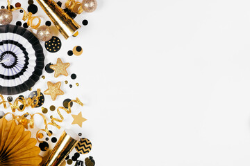 New Years Eve side border of gold and black confetti, noisemakers, streamers and decorations. Top down view on a white background.