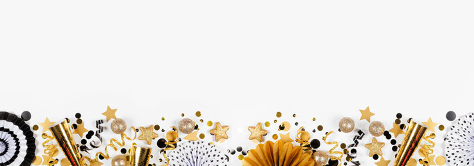 New Years Eve bottom border of gold and black confetti, noisemakers, streamers and decorations. Top view on a white banner background.