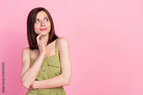 Portrait of optimistic minded woman dressed khaki overall finger on chin looking at empty space banner isolated on pink color background