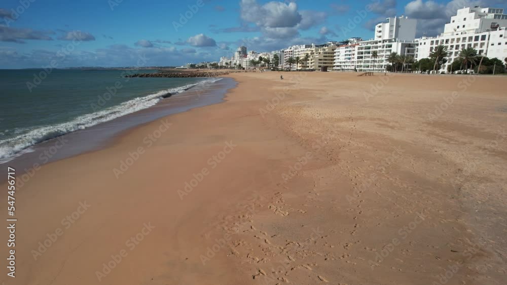 Aerial POV view of Quarteira beach, Portugal on a sunny day with waves crashing Aerial POV view of Quarteira beach, Portugal on a sunny day with waves crashing