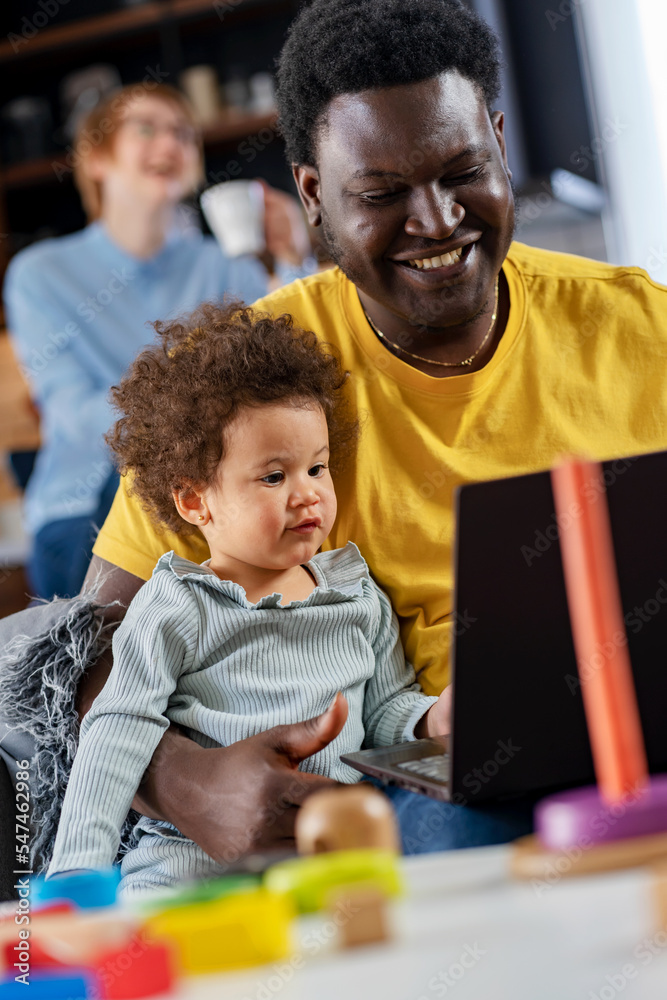 Father spends time with a cute daughter watching a laptop computer with her. Multicultural family. Educational apps for small kids.