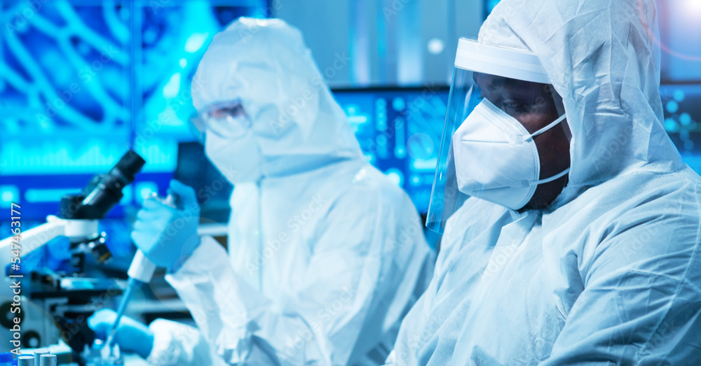 Fototapeta premium African-american doctor in protective suit is doing a science experiments and developing vaccine in a modern lab. Laboratory assistant workplace. The concept of science and medicine.