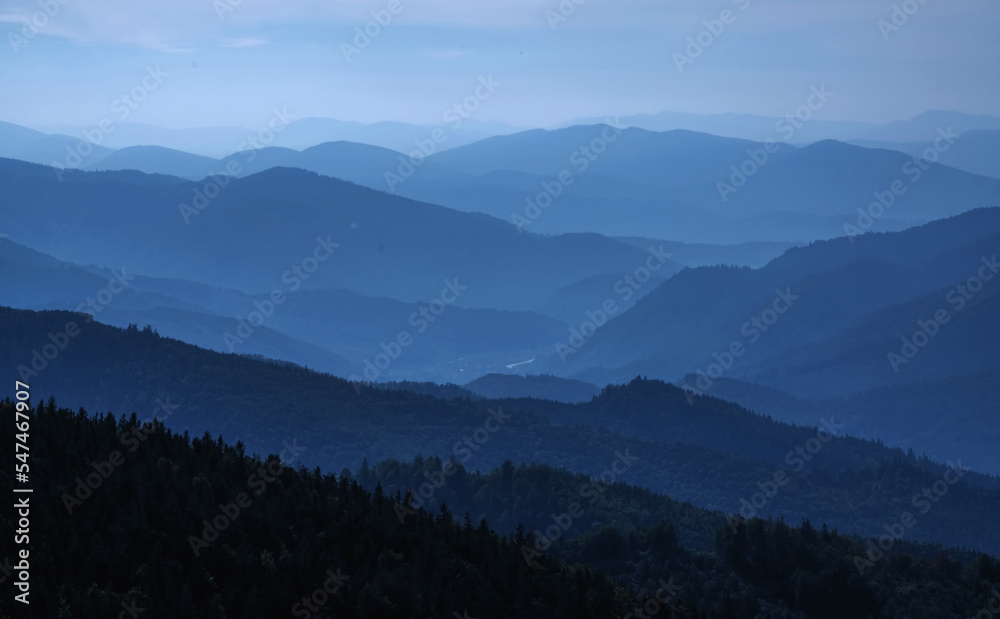 High peaks of beautiful dark blue mountain range landscape with fog and forest. Horizontal image.