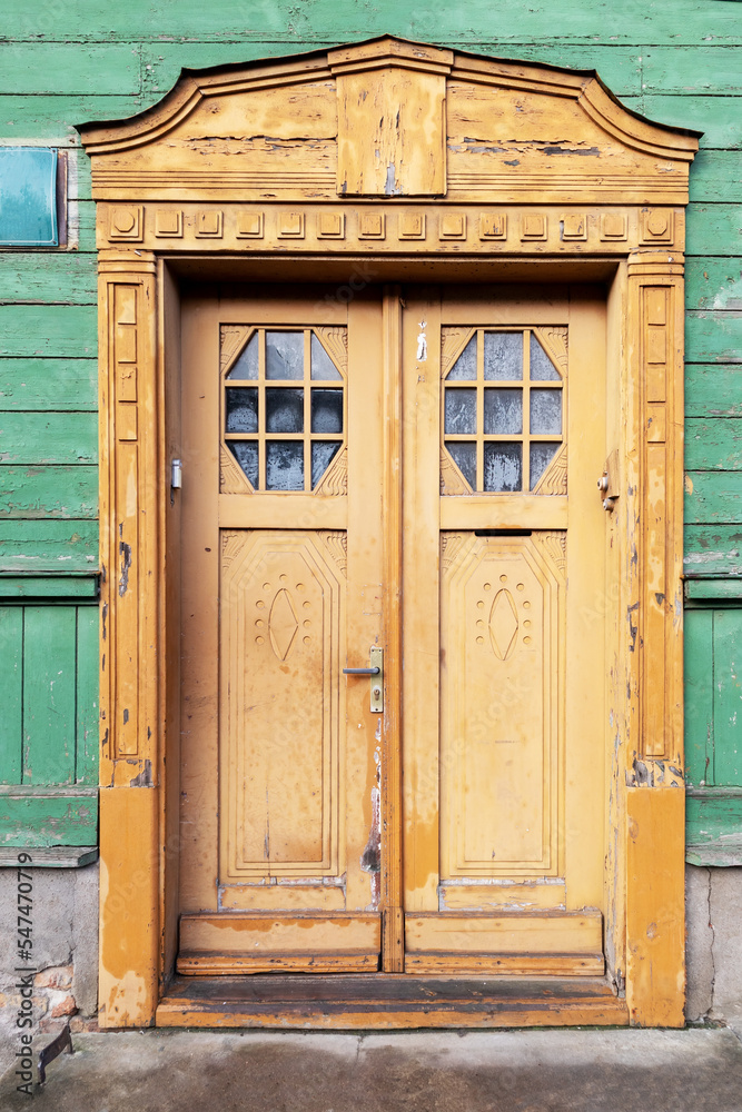 Painted old wooden door with carvings and two glass panes in a green house wall