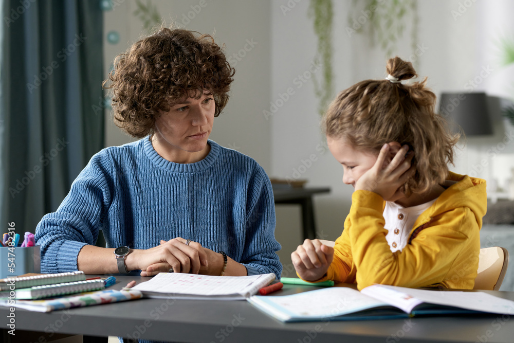 Young teacher teaching difficult child at home, they sitting together at desk with books and talking Young teacher teaching difficult child at home, they sitting together at desk with books and talking
