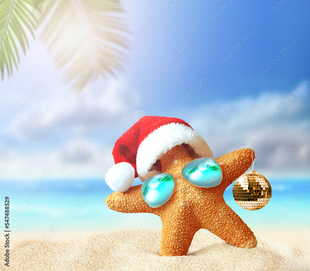 Starfish in Santa Claus hat and christmas ball on a summer beach. Merry Christmas - obrazy, fototapety, plakaty 