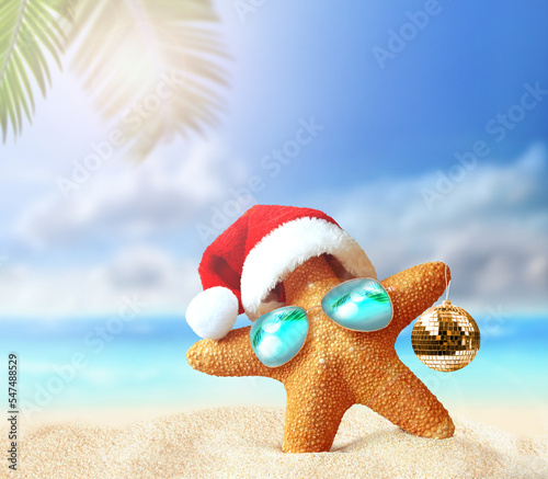 Starfish in Santa Claus hat and christmas ball on a summer beach. Merry Christmas