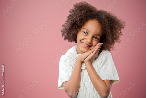 Portrait of cute Young African American child, over pink studio background. Eye contact. Cute girl 7 year old. Childhood, good mood, kindness  concept.