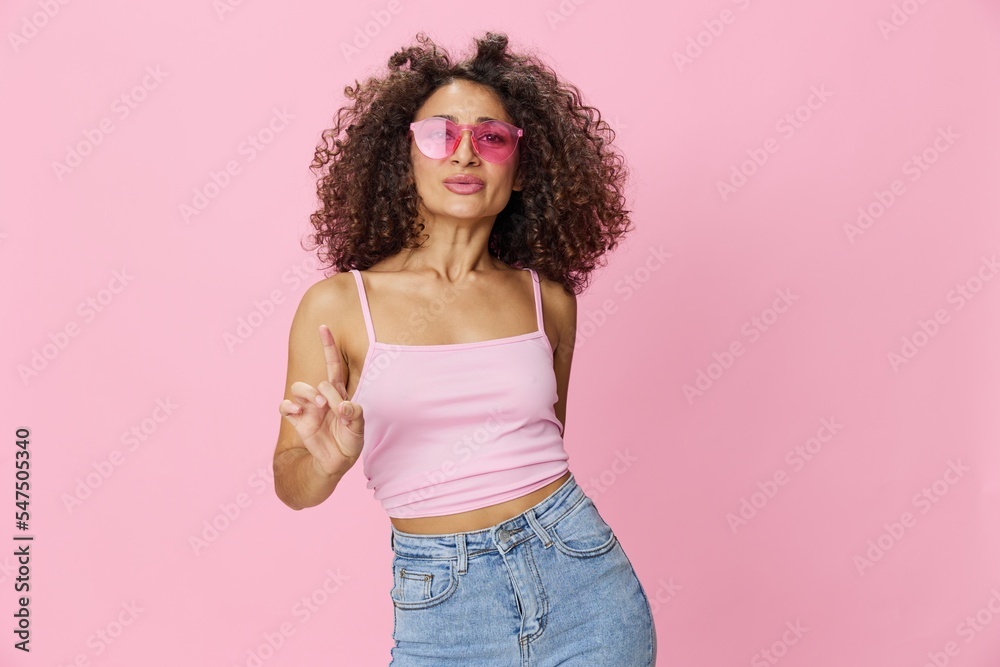 Happy woman afro curls hair dancing on pink background smile with teeth in summer pink t-shirt jeans and glasses, summer vibe, copy space Happy woman afro curls hair dancing on pink background smile with teeth in summer pink t-shirt jeans and glasses, summer vibe, copy space