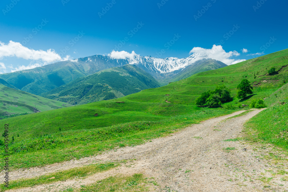 a path in the green valley of the Karmadon gorge with a view of the Kolka glacier of the Kazbek volcano of the main Caucasian ridge. Russia