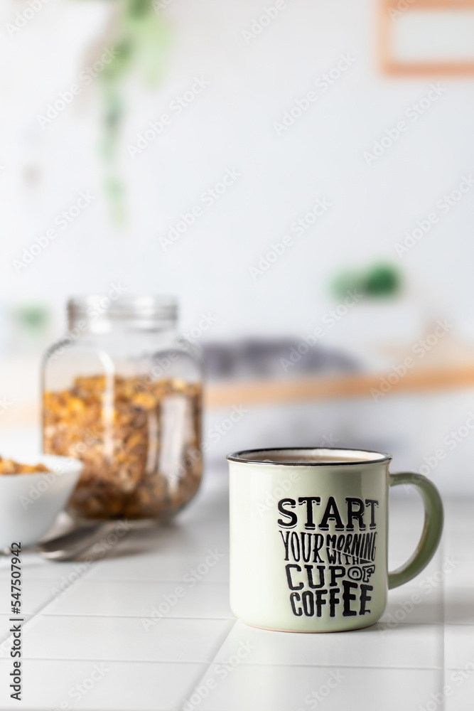 Mug of morning coffee on white tile tabletop in kitchen. Healthy breakfast consept with coffee and muesli. Text space Mug of morning coffee on white tile tabletop in kitchen. Healthy breakfast consept with coffee and muesli. Text space