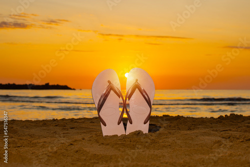 Flip flops stuck in the sand on the beach with the sun in the middle as dawn occurs. vacation concept