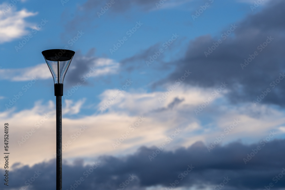 Bright blue cool autumn sky with some light airy transparent clouds where there are some dark dramatic clouds but in the middle a big black lantern on a pole.