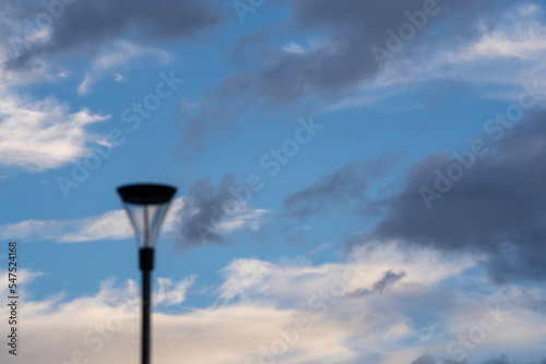 Bright blue cool autumn sky with some light airy transparent clouds where there are some dark dramatic clouds but in the middle a big black lantern on a pole.