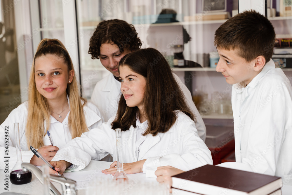 Fototapeta premium Discussion with a teacher at a chemistry lesson in a laboratory. Group of classmates are discussing chemistry experiments and homework at school. Education concept.